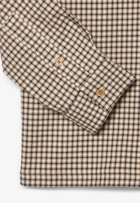 Beżowa i granatowa koszula w kratę z mankietami na guziki, z bawełnianego materiału, z klasycznym wzorem w kratkę o równych odstępach kwadratów.