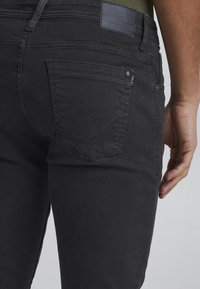 Vaqueros de mezclilla negra con corte ajustado. Incluye un bolsillo recto con costuras visibles y una etiqueta de cuero con logo en la parte trasera.