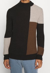 Stickad tröja med hög krage, prydd med block i svart, brunt och beige, ribbat mönster och åtsittande ärmslut.