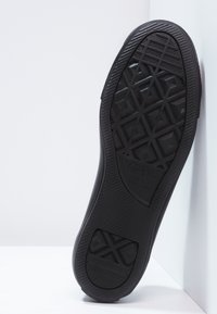 Semelle de chaussure en caoutchouc noir avec un motif de bande de roulement géométrique, présentant une surface texturée et un détail de logo. La semelle montre un design à bord incurvé.