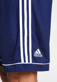 Shorts de sport bleu marine en tissu respirant, avec trois bandes blanches sur le côté et un logo Adidas blanc près de l'ourlet.
