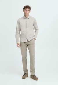 Lysfarget skjorte med knapper og teksturert mønster, lange ermer og krage. Kombinert med lysebeige bukser og brune sko.