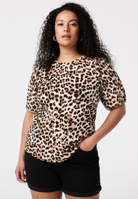 Blouse à manches courtes imprimé léopard avec un col rond, dotée de manches bouffantes et d'un tissu doux et texturé. Portée avec un short noir.