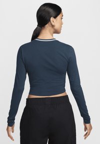 Bluză scurtă cu mânecă lungă din bumbac albastru închis, cu guler în dungi albe și textură ușoară. Asortată cu pantaloni negri cu talie elastică.