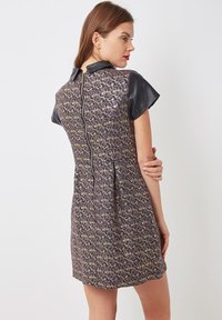 Vestido de manga corta con un patrón floral en dorado y púrpura, cuello de cuero negro y cremallera oculta en la parte posterior.