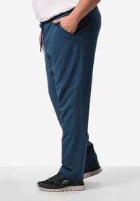 Blaue Jogginghosen mit einem elastischen Bund, seitlichen Taschen und geradem Schnitt, kombiniert mit schwarzen Sportschuhen mit einer leichten Sohle.