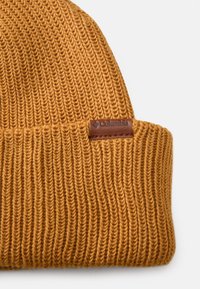 Knitted mustard-yellow beanie with a ribbed texture and a brown leather label featuring the Columbia logo on the folded brim.