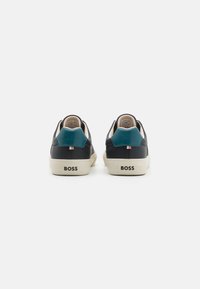 Zwarte leren sneakers met een teal accent op de hak, crème zool en "BOSS" logo op de achterkant. Gladde textuur met een gevoerde kraag.