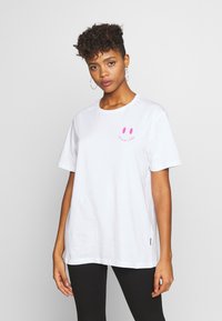 White cotton t-shirt with short sleeves, featuring a pink smiley face graphic and text. Casual fit, round neck, and minimal design details.