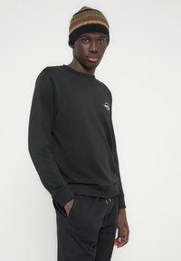 Μαύρο φούτερ από μαλακό ύφασμα, με στρογγυλή λαιμόκοψη και μακριά μανίκια. Συνδυασμένο με μαύρο παντελόνι και πλεκτό σκουφάκι με πολύχρωμες ρίγες.