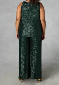 Grön paljett topp och vida byxor. Har en slät, texturerad yta med ljusreflekterande paljetter. Guldtonade skor synliga.