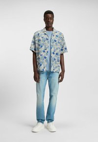 Lyhythihainen kukkakuvioinen paita, jossa on sinisiä ja valkoisia kuvioita, pukuna vaaleansinisellä t-paidalla, yhdistettyinä vaaleansinisiin farkkuihin ja valkoisiin lenkkareihin.