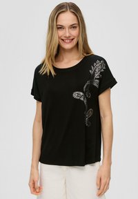 Czarna koszulka z krótkim rękawem, wykonana z miękkiej bawełny, z wzorem paisley w srebrnym kolorze po lewej stronie, o luźnym kroju i okrągłym dekolcie.