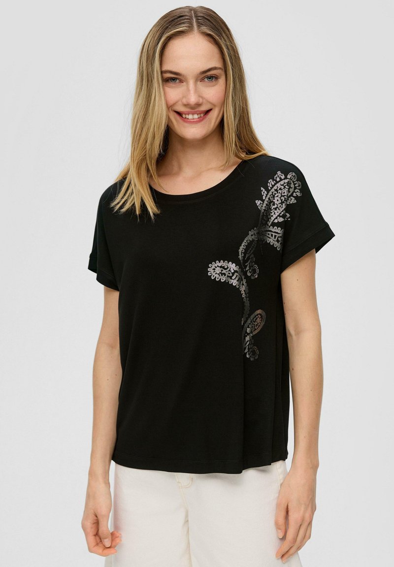 Czarna koszulka z krótkim rękawem, wykonana z miękkiej bawełny, z wzorem paisley w srebrnym kolorze po lewej stronie, o luźnym kroju i okrągłym dekolcie.