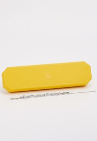 Yellow rectangular jewelry box with embossed logo and a silver bracelet featuring circular and beaded accents, reflecting light.
