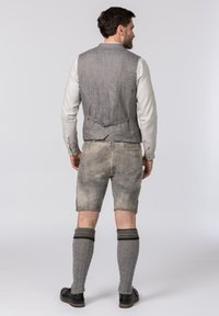 Graue Leinenweste über einem weißen Langarmhemd, kombiniert mit grauen Shorts, knielangen grauen gemusterten Socken und schwarzen Schuhen.