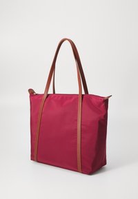Tote bag in vibrant burgundy fabric with brown leather straps. Features a zip closure, rectangular shape, and smooth texture.