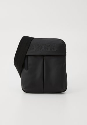 Black crossbody bag made of smooth synthetic material. Features a front flap with an embossed logo and a woven strap for easy carrying.