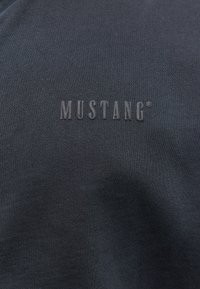 Dark gray cotton T-shirt featuring a textured, embossed "MUSTANG" logo on the chest. Smooth fabric with fine ribbing.