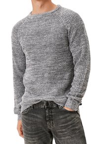 Grau-weißes Strickpullover mit gerippten Bündchen und Kragen, mit einem strukturierten Muster. Kombiniert mit dunkelgrauen Jeans.