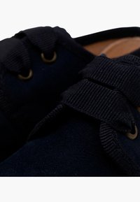 Tyrkysově modré semišové boty s kulatými tkaničkami, kovovými očky a texturovaným jazykem. Detailní záběr zdůrazňující detaily.