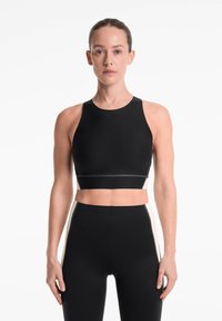 Top court noir avec encolure haute, design sans couture et silhouette ajustée. Assorti à un legging noir taille haute avec des accents sur les côtés.