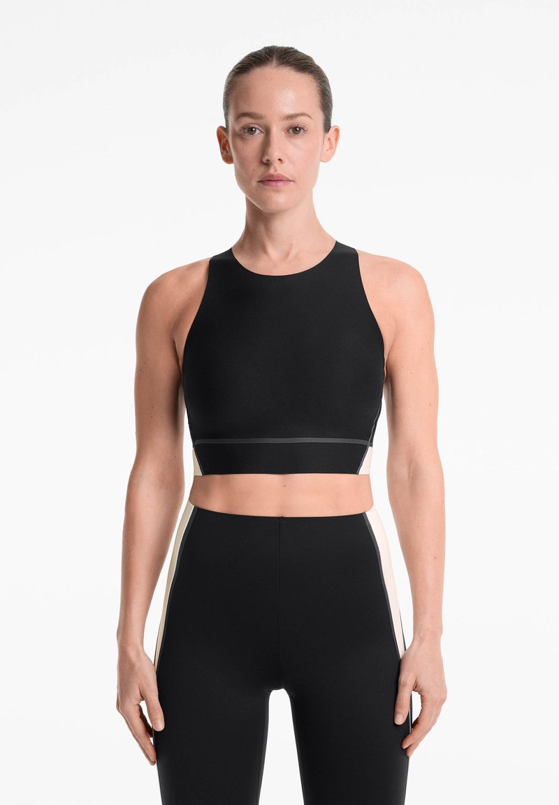 Top court noir avec encolure haute, design sans couture et silhouette ajustée. Assorti à un legging noir taille haute avec des accents sur les côtés.