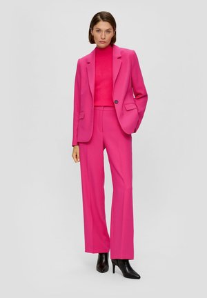 Fuchsia suit with a tailored blazer and wide-leg trousers. Textured knit turtleneck underneath. Black pointed-toe boots complement the outfit.