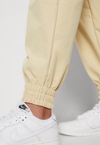 Light yellow jogger pants with elastic cuffs, made of soft cotton, paired with white Nike sneakers featuring a black logo.