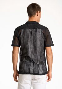 Camisa negra de manga corta hecha de un tejido de malla texturizado, con un patrón a rayas y una banda sólida en el cuello.