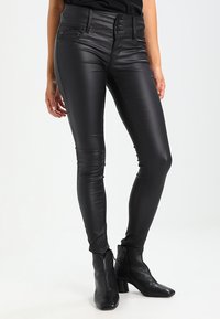 Pantalon skinny en simili cuir noir avec une taille haute, équipé d'une fermeture à bouton et de détails de couture le long des coutures.