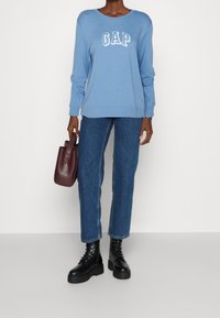 Sudadera azul clara con el logo "GAP", combinada con jeans rectos de mezclilla oscura y botas de plataforma negras con cordones. Sosteniendo un bolso burdeos.