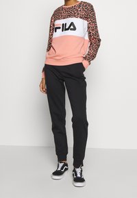 Felpa rosa chiaro con maniche a stampa leopardata e grande logo "FILA" nero, abbinata a pantaloni neri tapered e sneakers nere.