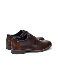 Zapatos de cuero marrón con un acabado suave, punta redonda y costuras distintivas. Presenta un diseño de cordones y suelas de goma.