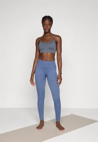 Grå sports-BH og blå leggings laget av glatt stoff, med en tettsittende design med ribbestruktur og elastisk midjebånd.