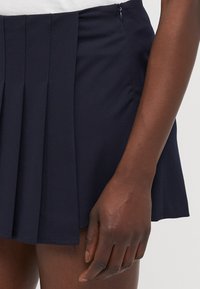 Navy blue pleated skirt made of lightweight fabric, featuring a side zipper and a flared design, visible textured pleats along the waistband.