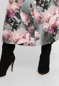 Šaty s květinovým vzorem, na světle modrém pozadí s růžovými růžemi, doplněné černými semišovými vysokými botami na podpatku do půli lýtek.