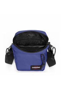 Blå tyg crossbody-väska med dragkedjestängning, justerbar axelrem och innerfickor; har ett framträdande Eastpak-logomärke.