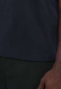T-shirt in cotone blu navy con un logo goffrato discreto, maniche corte e orlo dritto. Il tessuto ha una texture liscia.