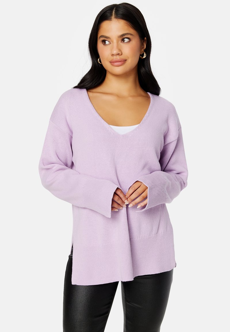Maglione lilla in un morbido tessuto a maglia, con scollo a V, vestibilità ampia e maniche lunghe con dettagli a costine. Abbinato a pantaloni attillati neri.
