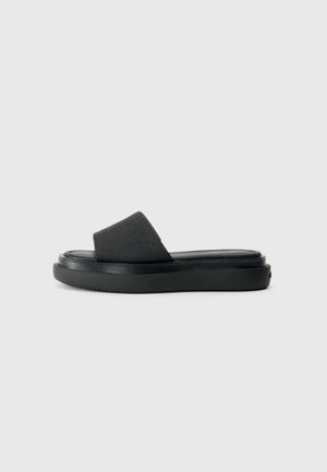 Sorte slip-on sandaler med en tekstureret stofoverdel, bred rem og en tyk gummisål, der har en glat overflade og minimalistisk design.