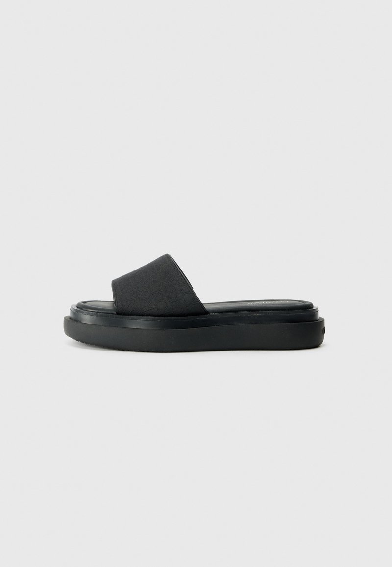 Sandales noires à enfiler avec un dessus en tissu texturé, une large sangle et une semelle en caoutchouc épaisse, présentant une finition lisse et un design minimaliste.