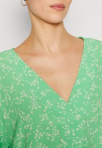 Grønn v-hals bluse med et blomsterdesign i en lysere nyanse, laget av myk stoff med delikat søm og en avslappet passform.