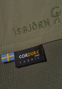 Olivgrön tyg med "ISBJÖRN" broderat i matchande tråd, med en märkning som visar "CORDURA®" i svart och orange.