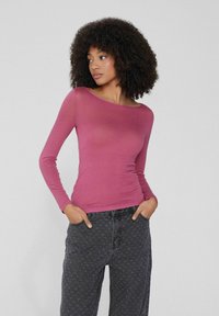 Dlouhý rukáv, přiléhavý top z měkkého, lehkého fialového materiálu s širokým výstřihem. V kombinaci s tmavými vzorovanými džíny s vysokým pasem.