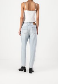 Ljusblå, högmidjade jeans med avslappnad passform, som har fickor med lappar, en brun läderetikett och svarta klackskor med blockklack. Vit ribbad tanktop.