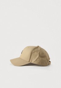 Μπεζ καπέλο του μπέιζμπολ κατασκευασμένο από υφασμα με υφή, με καμπυλωτό γείσο και ρυθμιζόμενο λουράκι στο πίσω μέρος. Μινιμαλιστικός σχεδιασμός χωρίς σχέδια.