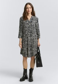 Zwart-wit gestreepte jurk met lange mouwen en een kraag, gestyled met zwarte enkellaarzen en een zwarte handtas. Zacht materiaal, losse pasvorm.