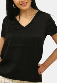 Top corto nero a maniche corte con scollatura a V, tessuto morbido e vestibilità ampia. Presenta una cucitura orizzontale e cerniere laterali discrete all'orlo.