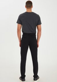 Svarta skräddarsydda byxor med slim fit, tillverkade av smidigt tyg, med sidfickor och doldt midjeband. Bärs med en grå t-shirt.